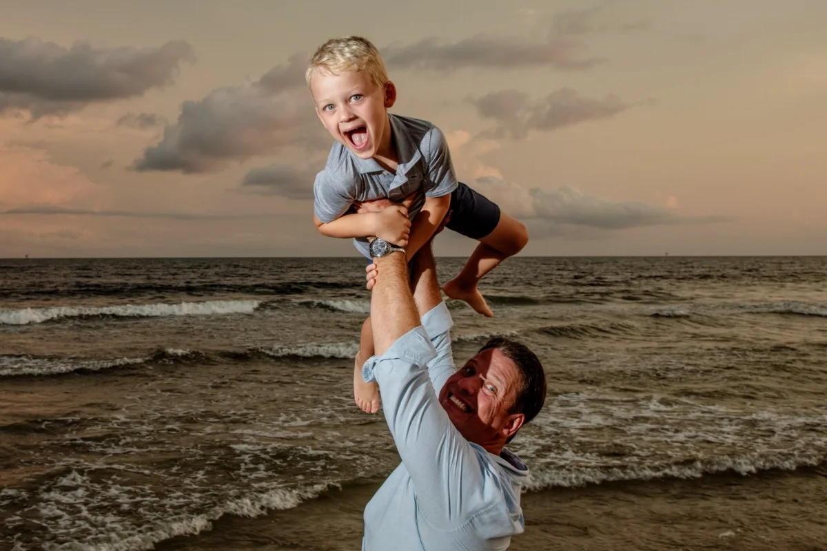Orange beach photographer Sample Photos 16 Dad holding the baby up in the air down by the beach during an Orange Beach family portrait session.