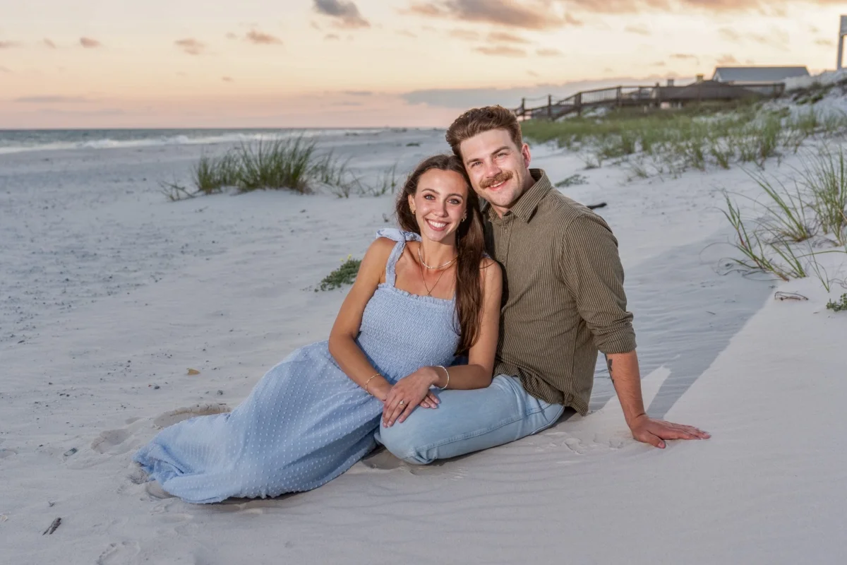 Young couple sitting on the sand by the edge of the water in Orange Beach, Alabama during a photo session.